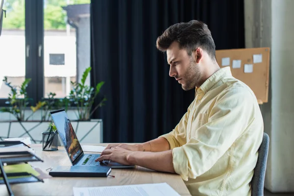 Side view of businessman using laptop near documents and notebook in office — Stock Photo