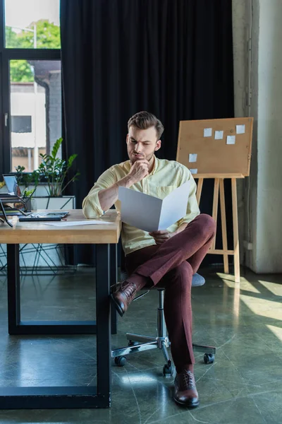 Thoughtful businessman looking at paper folder near laptop on table in office — Stock Photo