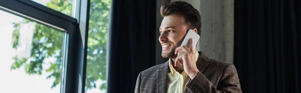 Cheerful manager talking on mobile phone near window in office, banner — Foto stock