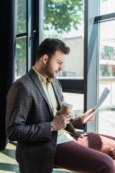 Side view of businessman holding contract and paper cup in office — Fotografia de Stock