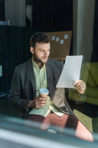 Businessman looking at paper and holding takeaway coffee in office — Photo de stock