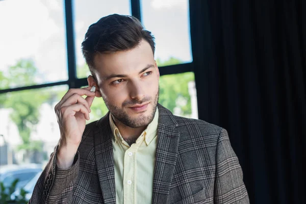 Businessman holding earphone and looking away in office — Stock Photo