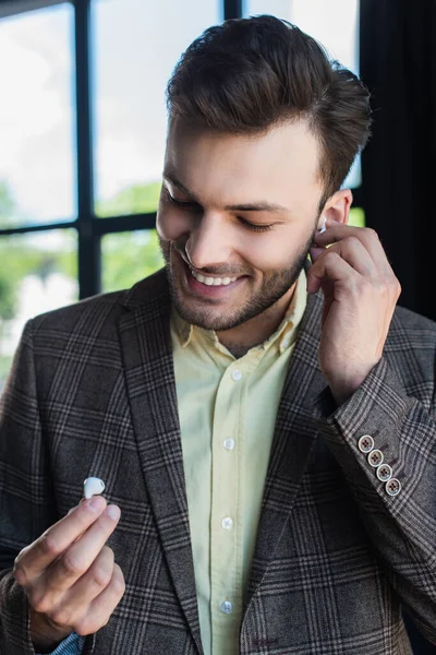 Smiling businessman in jacket holding earphones in office — Stock Photo