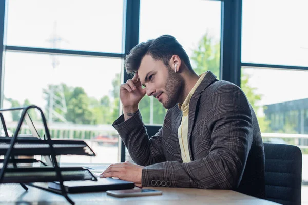 Вид збоку бізнесмена в навушниках, використовуючи ноутбук біля розмитих паперів в офісі — стокове фото
