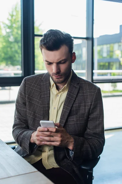Бизнесмен в куртке с помощью смартфона в офисе — стоковое фото