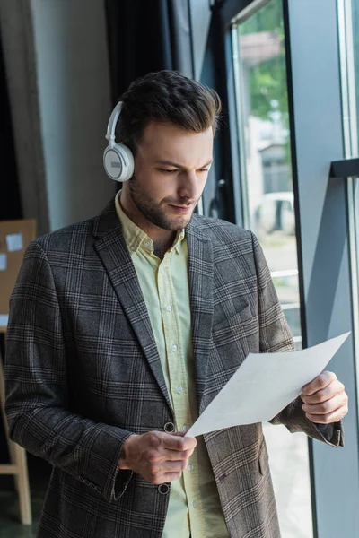 Young businessman in wireless headphones holding paper in office — Fotografia de Stock