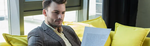 Young businessman looking at paper while sitting on couch in office, banner — Stock Photo