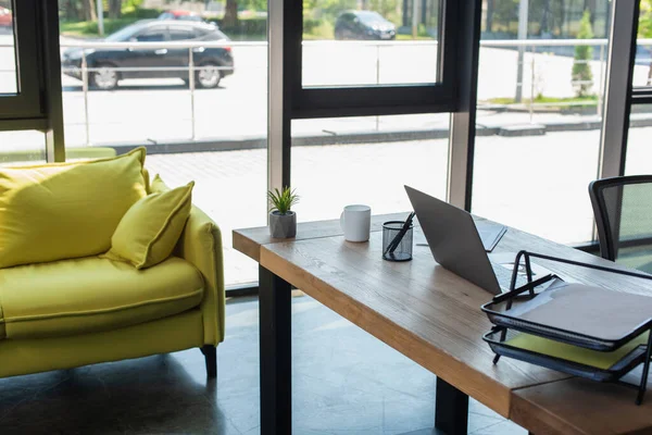 Papers and laptop on working table near couch in office — Photo de stock