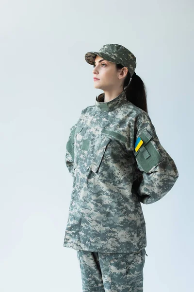 Young soldier in uniform with ukrainian flag looking away isolated on grey — стокове фото