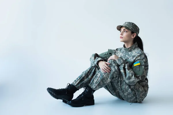 Soldier in military uniform with ukrainian flag sitting on grey background — Foto stock