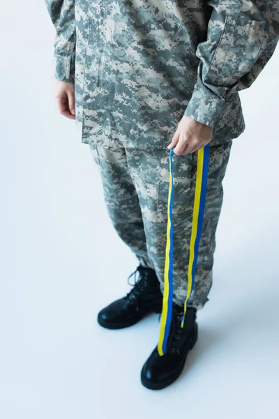 Обрізаний вид солдата, що тримає синьо-жовту стрічку на сірому фоні — стокове фото