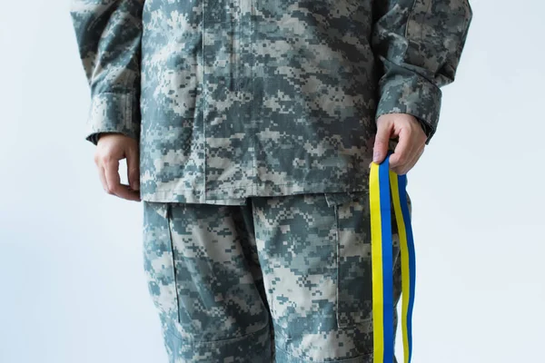 Cropped view of servicewoman holding blue and yellow ribbon isolated on grey — стоковое фото