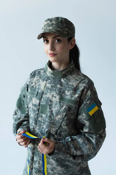 Soldier in cap and uniform holding blue and yellow ribbon isolated on grey — стоковое фото