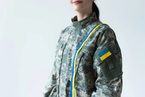 Cropped view of smiling soldier in uniform with blue and yellow ribbon and ukrainian flag isolated on grey — стокове фото