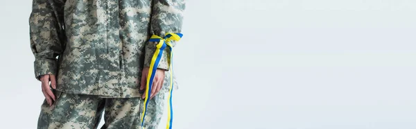 Cropped view of servicewoman in military uniform and blue and yellow ribbon on hand isolated on grey, banner — Fotografia de Stock