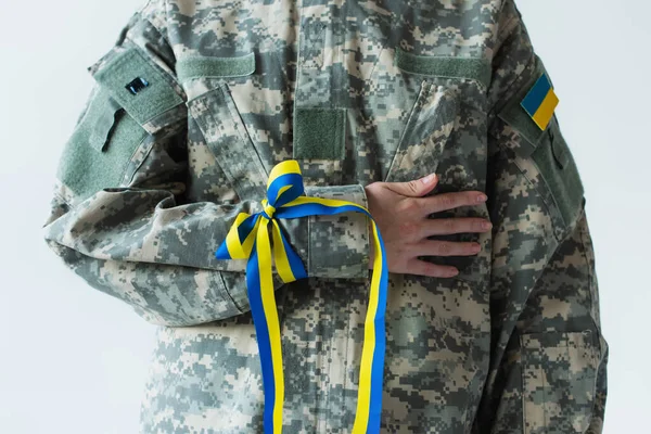 Cropped view of soldier with ukrainian flag and blue and yellow ribbon on hand isolated on grey — стокове фото