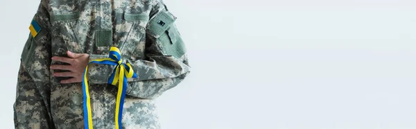 Cropped view of soldier with ukrainian flag on chevron and blue and yellow ribbon on hand isolated on grey, banner — Photo de stock