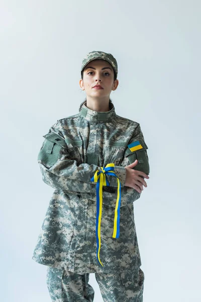 Soldier in uniform with ukrainian flag and blue and yellow ribbon crossing arms isolated on grey - foto de stock