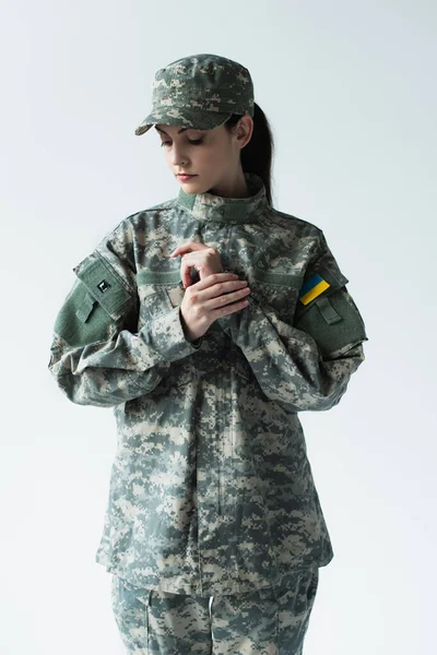 Soldier in camouflage uniform with ukrainian flag looking away isolated on grey — стокове фото