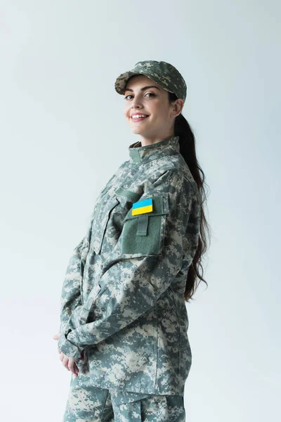 Positive soldier in cap and uniform with ukrainian flag isolated on grey — стоковое фото