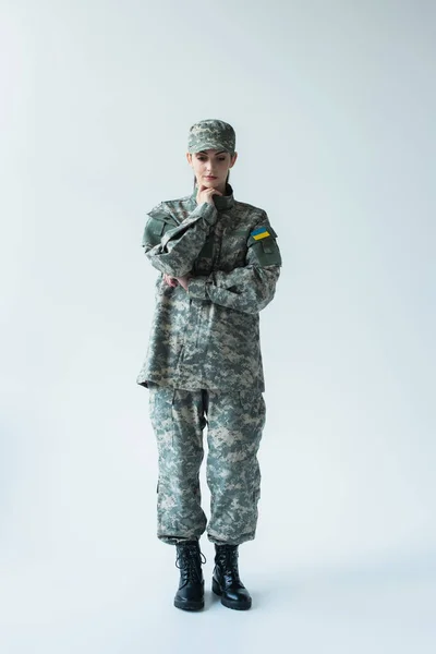 Full length of upset soldier in uniform with ukrainian flag on grey background — Photo de stock