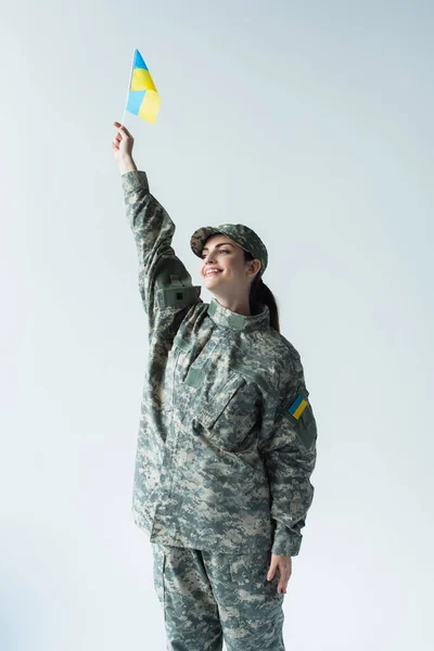 Smiling soldier in uniform rising ukrainian flag isolated on grey — Fotografia de Stock