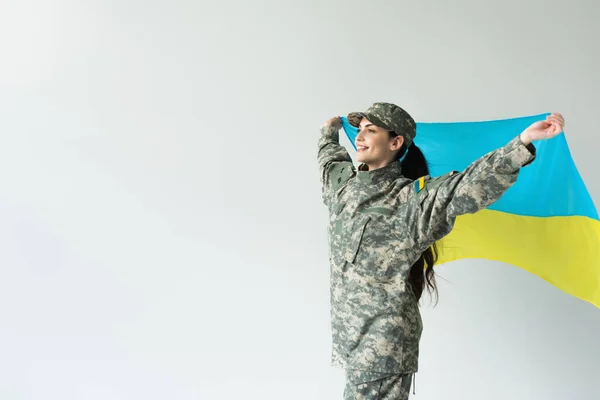 Happy servicewoman holding ukrainian flag isolated on grey — Photo de stock