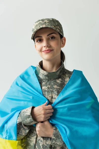 Portrait of smiling soldier covering with ukraining flag isolated on grey — Stock Photo