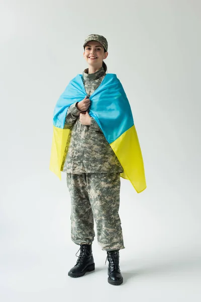 Happy soldier covering with ukrainian flag on grey background — Stockfoto