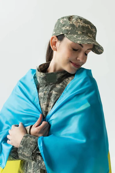 Young soldier in uniform covering with ukrainian flag isolated on grey — Fotografia de Stock