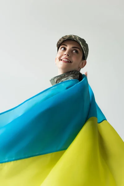 Smiling soldier in uniform and ukrainian flag looking away isolated on grey — стокове фото