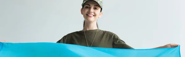 Cheerful servicewoman in uniform holding blue cloth isolated on grey, banner — Stock Photo