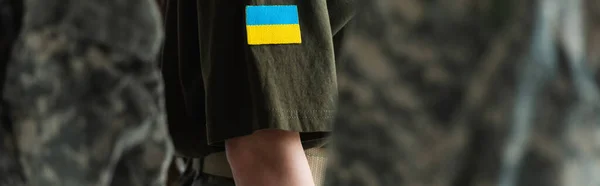 Cropped view of servicewoman with ukrainian flag on chevron standing near soldiers, banner — Fotografia de Stock