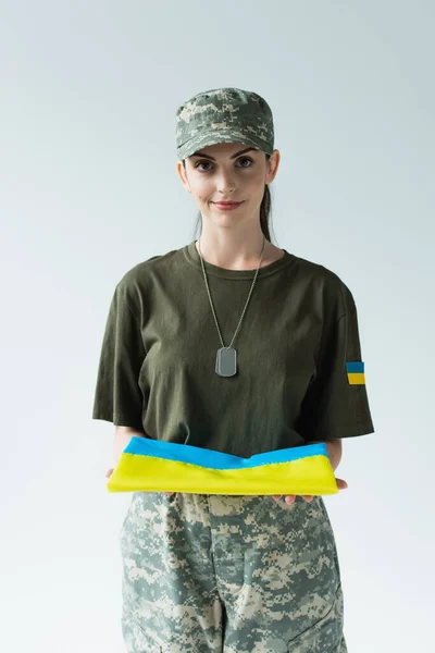 Smiling soldier holding ukrainian flag isolated on grey — стоковое фото