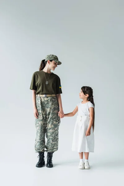 Side view of soldier with ukrainian flag on uniform holding hand of daughter on grey background — Stock Photo