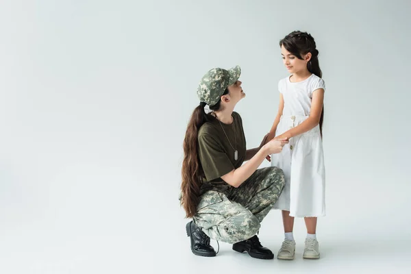 Smiling woman in military uniform holding hands of daughter on grey background — Stock Photo