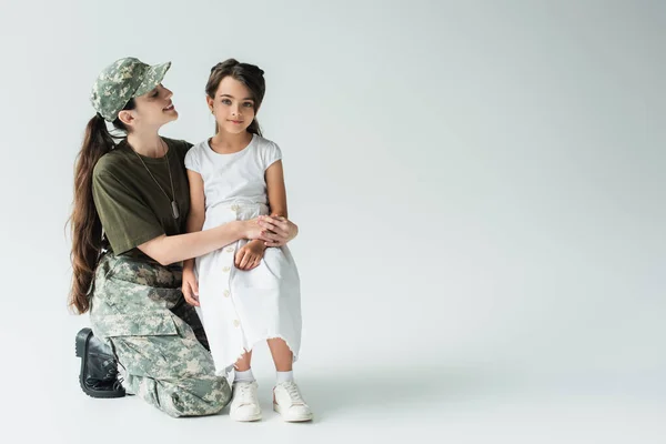 Positive mother in military uniform looking at child on grey background - foto de stock