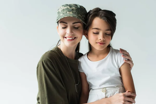 Mother in military uniform and daughter smiling and closing eyes isolated on grey - foto de stock