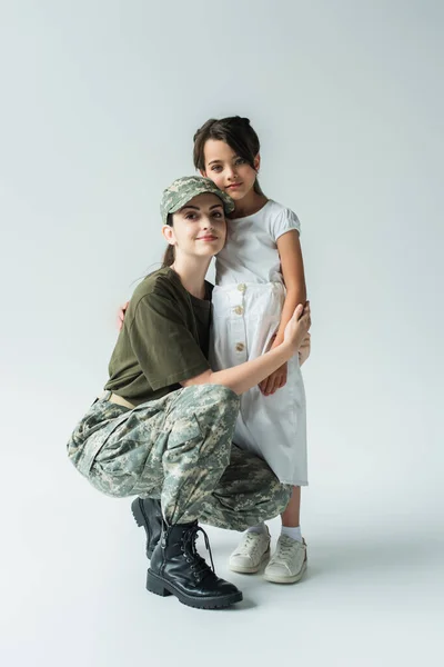 Молодий батько у військовій формі обіймає дочку на сірому фоні — стокове фото