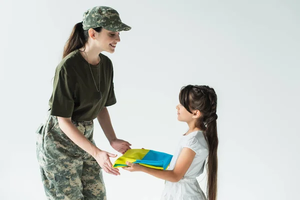 Child holding ukrainian flag near mom in camouflage uniform isolated on grey — Foto stock