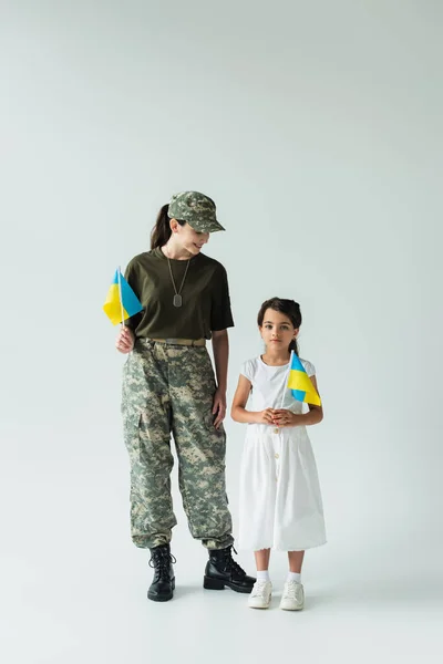 Soldier holding ukrainian flag near daughter on grey background — Foto stock