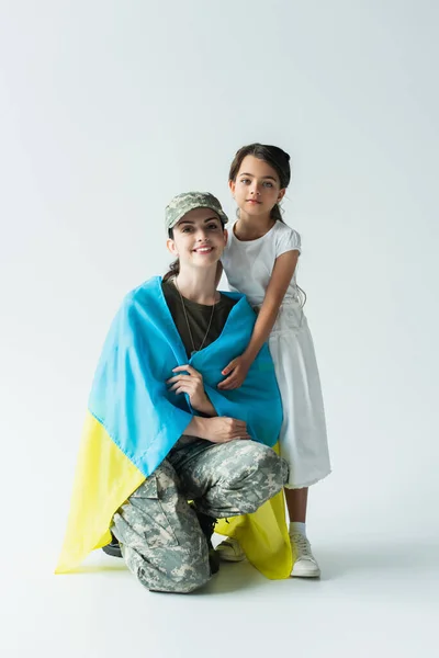 Kid hugging soldier in military uniform and ukrainian flag on grey background — стоковое фото