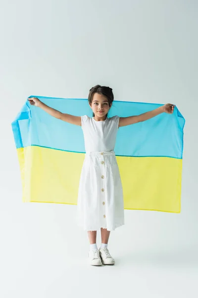 Kid holding ukrainian flag and looking at camera on grey background — Stock Photo