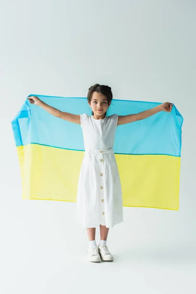Kid holding ukrainian flag and looking at camera on grey background — стоковое фото