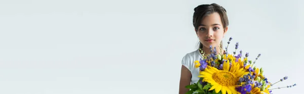 Girl looking at camera near blue and yellow flowers isolated on grey, banner — стоковое фото