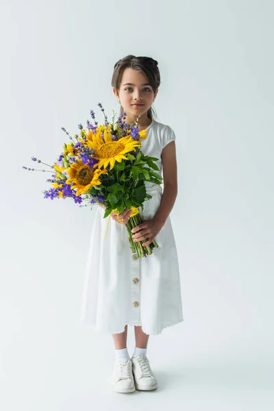 Full length of child holding blue and yellow bouquet on grey background — Fotografia de Stock