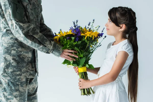 Child giving blue and yellow bouquet to servicewoman in camouflage uniform isolated on grey — Stock Photo