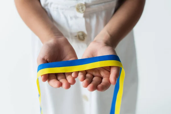 Обрізаний вид розмитої дівчини, що тримає синьо-жовту стрічку ізольовано на сірому — стокове фото