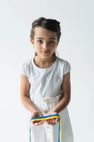 Дитина тримає синю рекламу жовту стрічку і дивиться на камеру ізольовано на сірому — стокове фото
