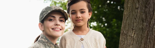 Happy woman in camouflage looking at camera near daughter outdoors, banner — Stockfoto